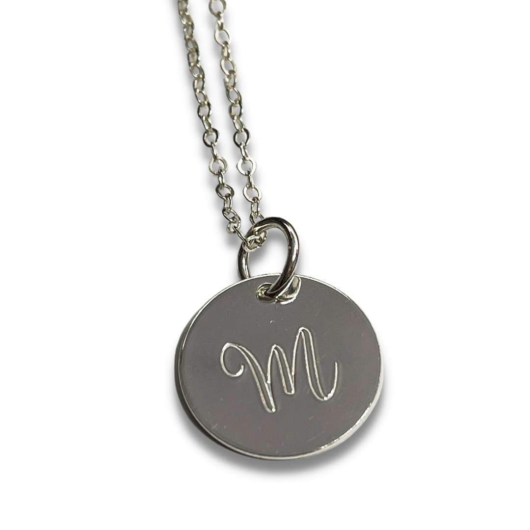Up Close Sterling silver Script Initial necklace laying on a heart shaped dish . Select the length of chain you would like as well as the metal type.