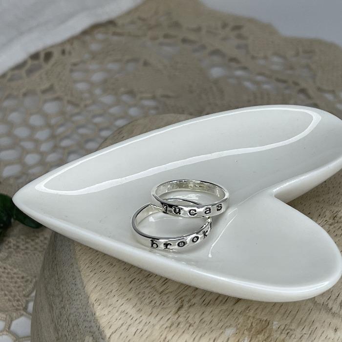 Two sterling silver inspiration rings sitting in a heart shaped dish. the names have been darkened so they can be seen easily