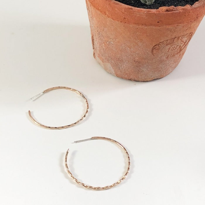 Gold Filled Crimp Hoops laying on the table beside a terracotta planter