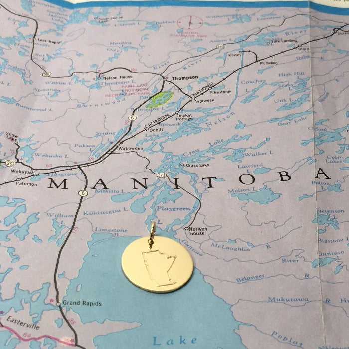 Gold hand stamped Manitoba necklace laying on a map