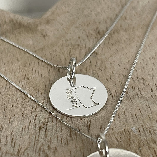 Mini Manitoba is stamped onto a 5/8 disk in either sterling or 14k gold fill.