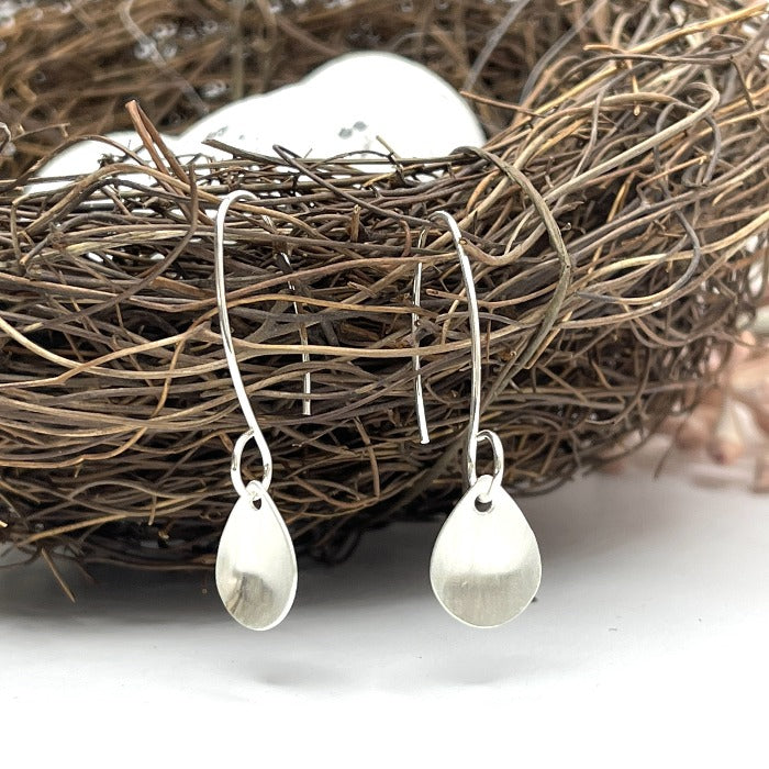 Brushed raindrop shaped sterling earrings hanging from a bird's nest