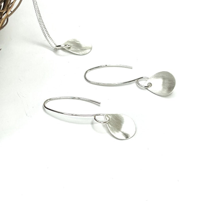 Brushed raindrop shaped sterling earrings laying on a white background