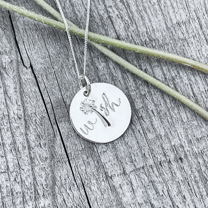 The hand stamped WISH necklace has laying with two dandeiions