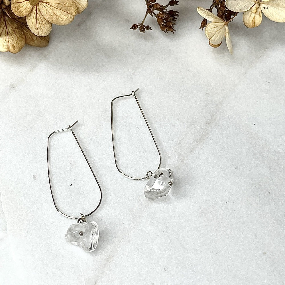 Crystal quartz dandle earrings laying on a marble slab, sterling silver hoop style