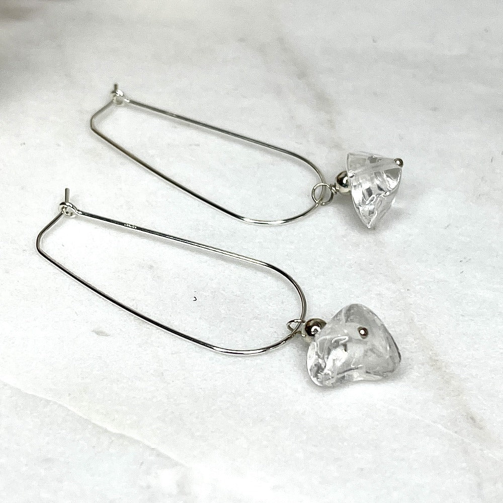 Crystal quartz dandle earrings laying on a marble slab, sterling silver hoop style