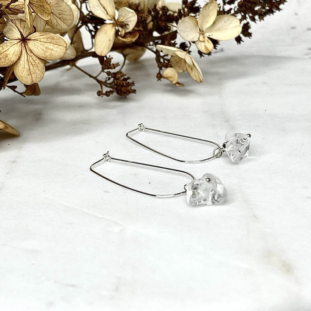 Crystal quartz dandle earrings laying on a marble slab, sterling silver hoop style