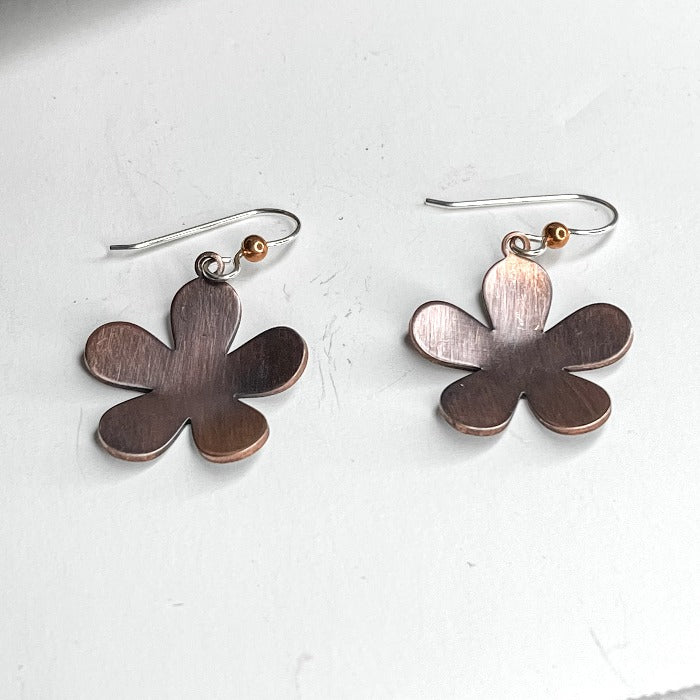 Copper floral /daisy shaped earrings that have been oxidized on a white background  Each pair is slightly different.
