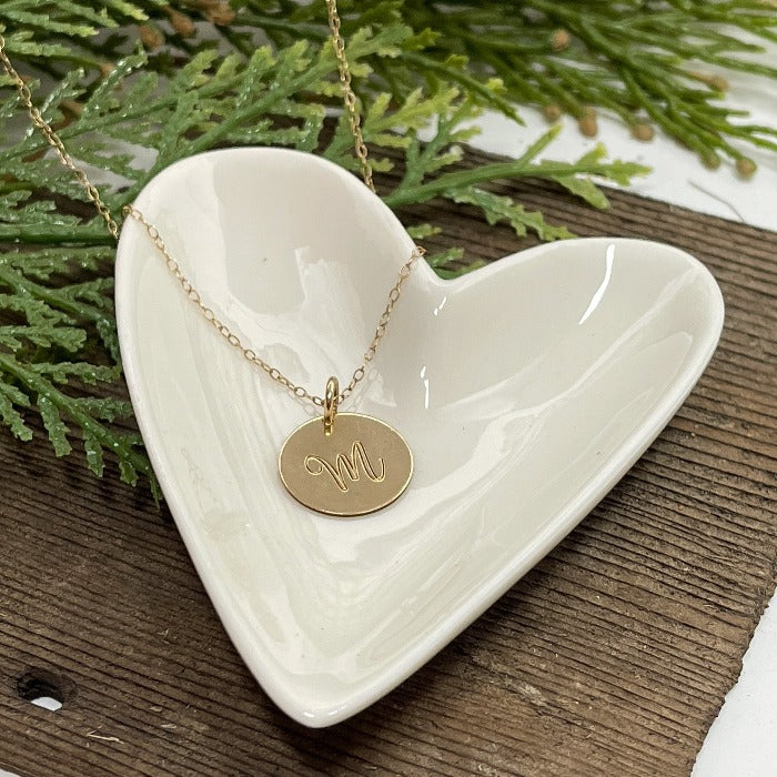 14K Gold-filled Script Initial necklace laying on a heart shaped dish .  Select the length of chain you would like as well as the metal type.