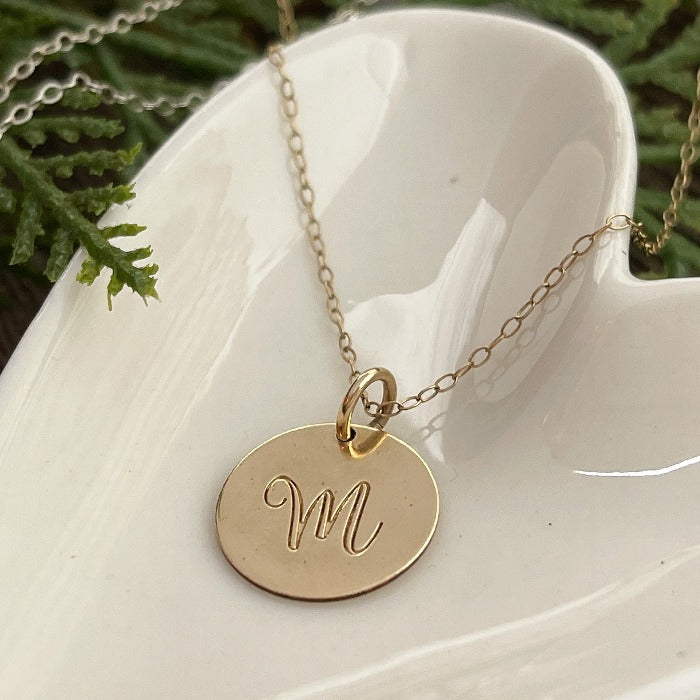 Up close 14K Gold-filled Script Initial necklace laying on a heart shaped dish .  Select the length of chain you would like as well as the metal type.
