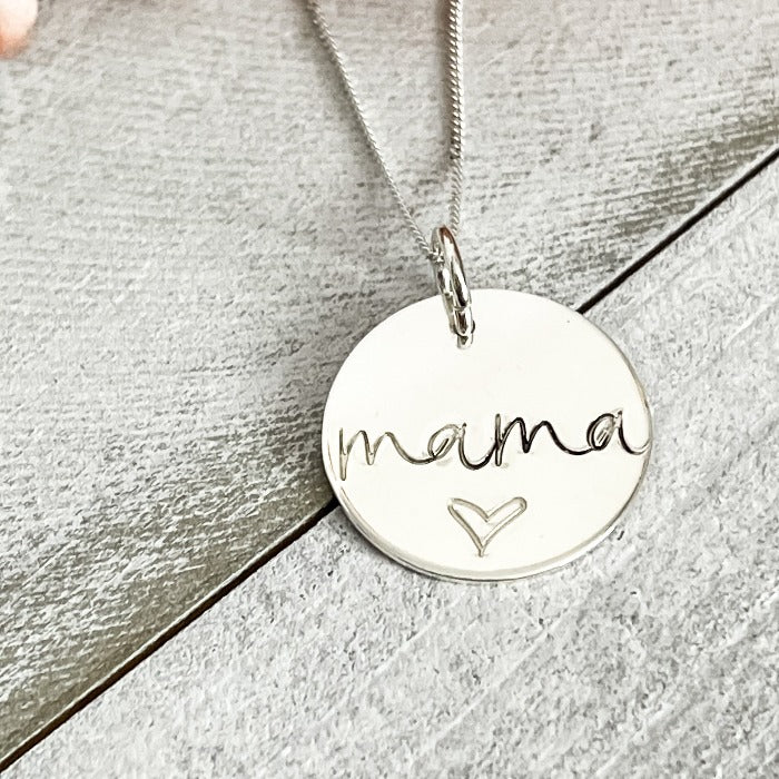 A sterling silver disk necklace with mama and a heart below it hand-stamped on it