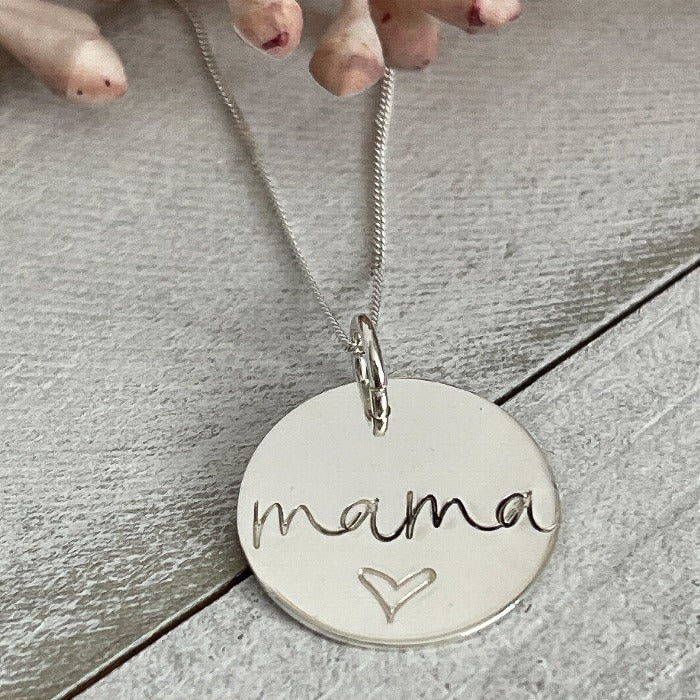 A sterling silver disk necklace with mama and a heart below it hand-stamped on it